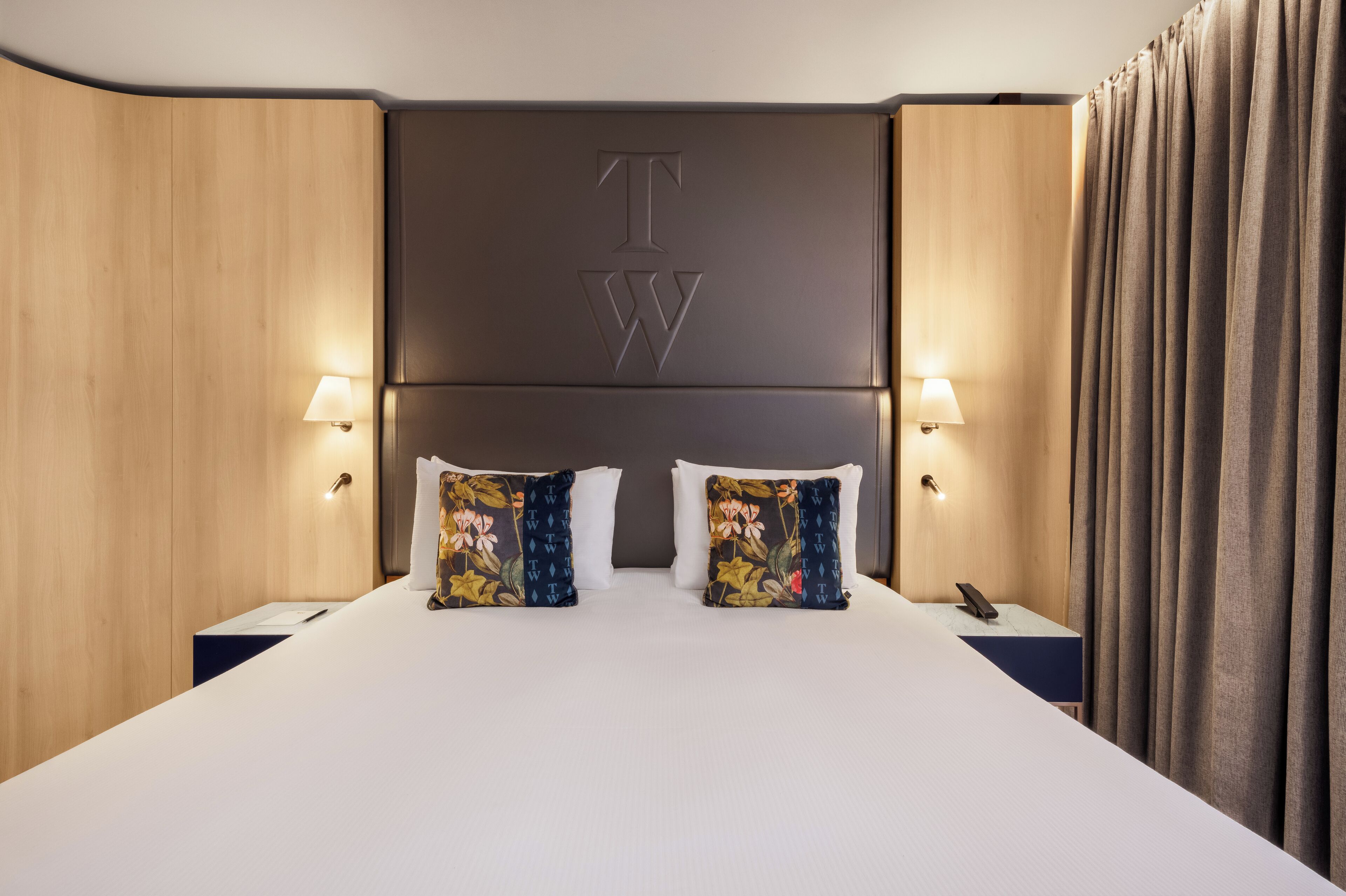 Habitación de hotel con una cama grande, dos mesitas de noche, una lámpara y una cortina.