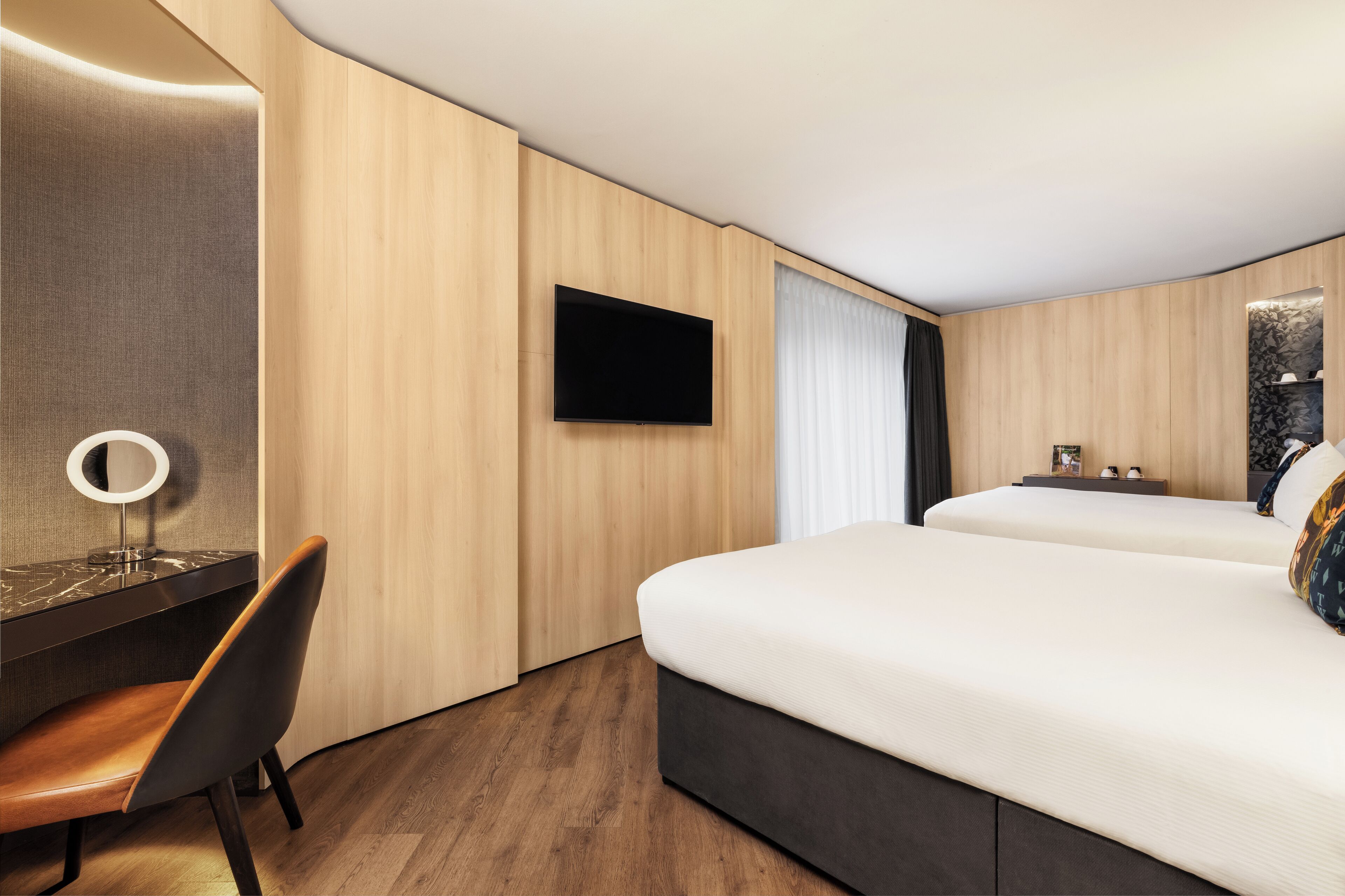 A hotel room with a bed, a desk with a chair, a television, and a mirror.