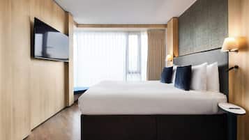 A modern hotel room with a large bed, a flat-screen TV mounted on the wall, and a small bedside table.