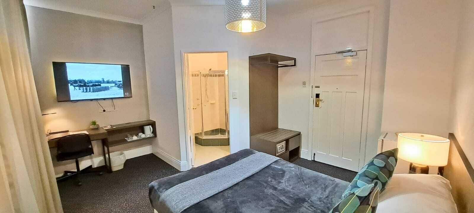 A hotel room with a bed, desk, TV, and a shower area.