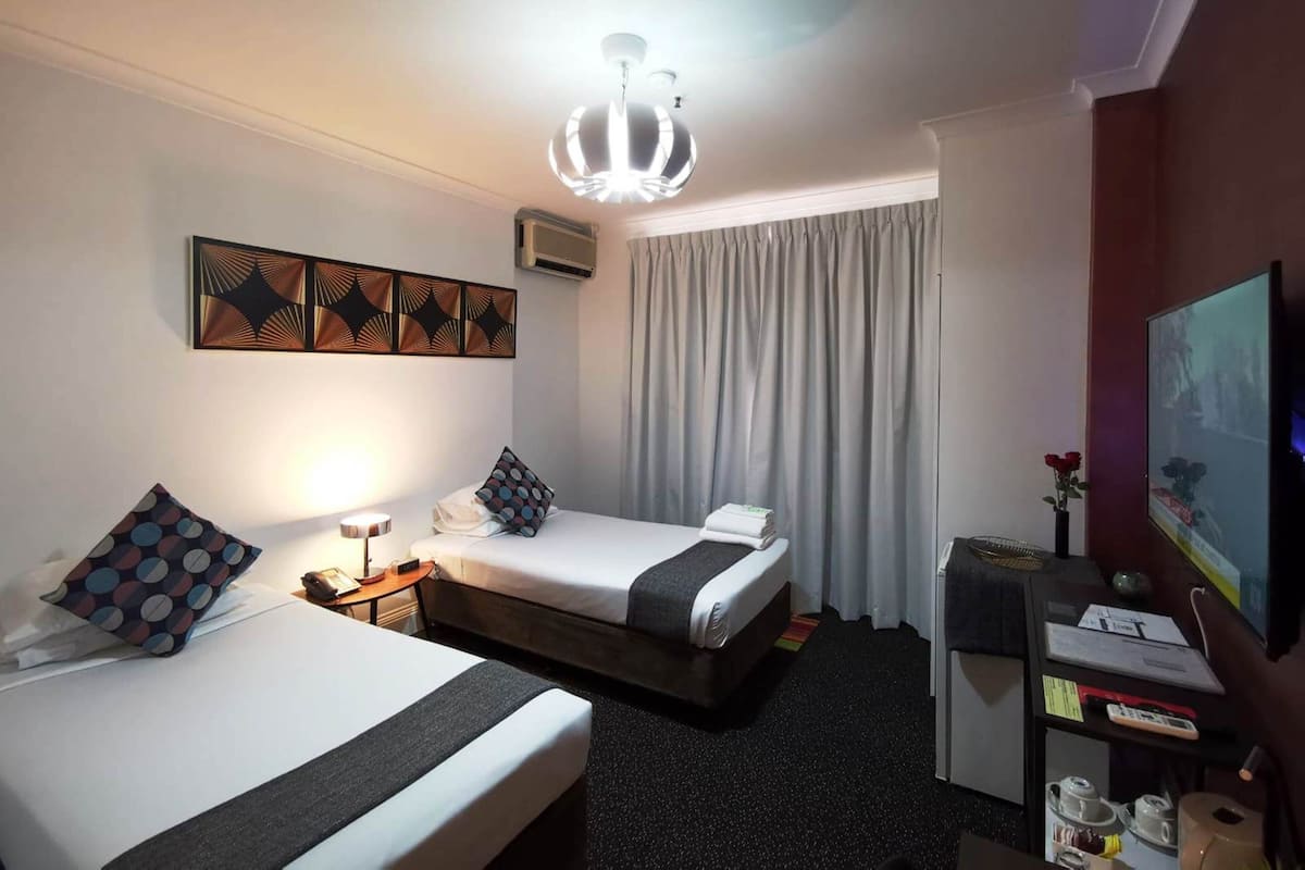 A hotel room with two beds, a ceiling fan, a TV, a desk with a computer, and a window with curtains.