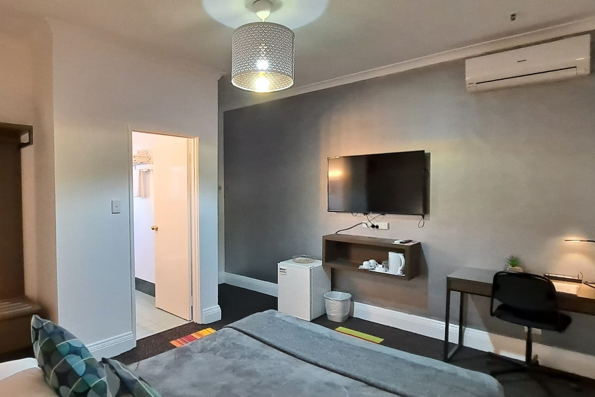 A hotel room with a bed, a desk, a chair, a TV, a lamp, and a wardrobe.