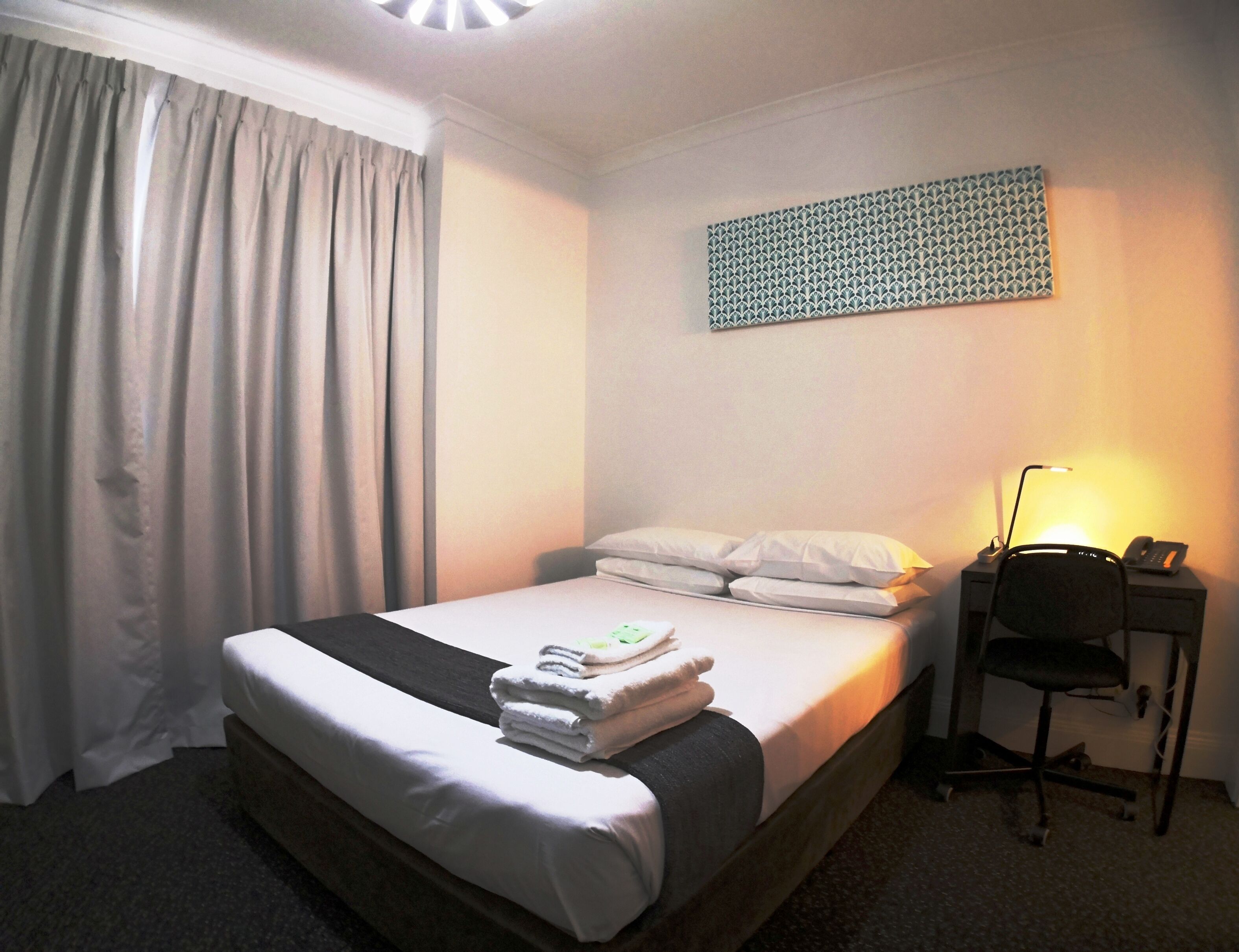 Habitación de hotel con cama, escritorio con silla, lámpara y teléfono en la pared.
