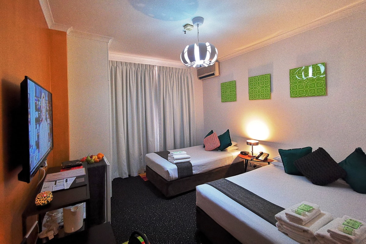 A hotel room with two beds, a TV, a desk, a lamp, and artwork on the walls.