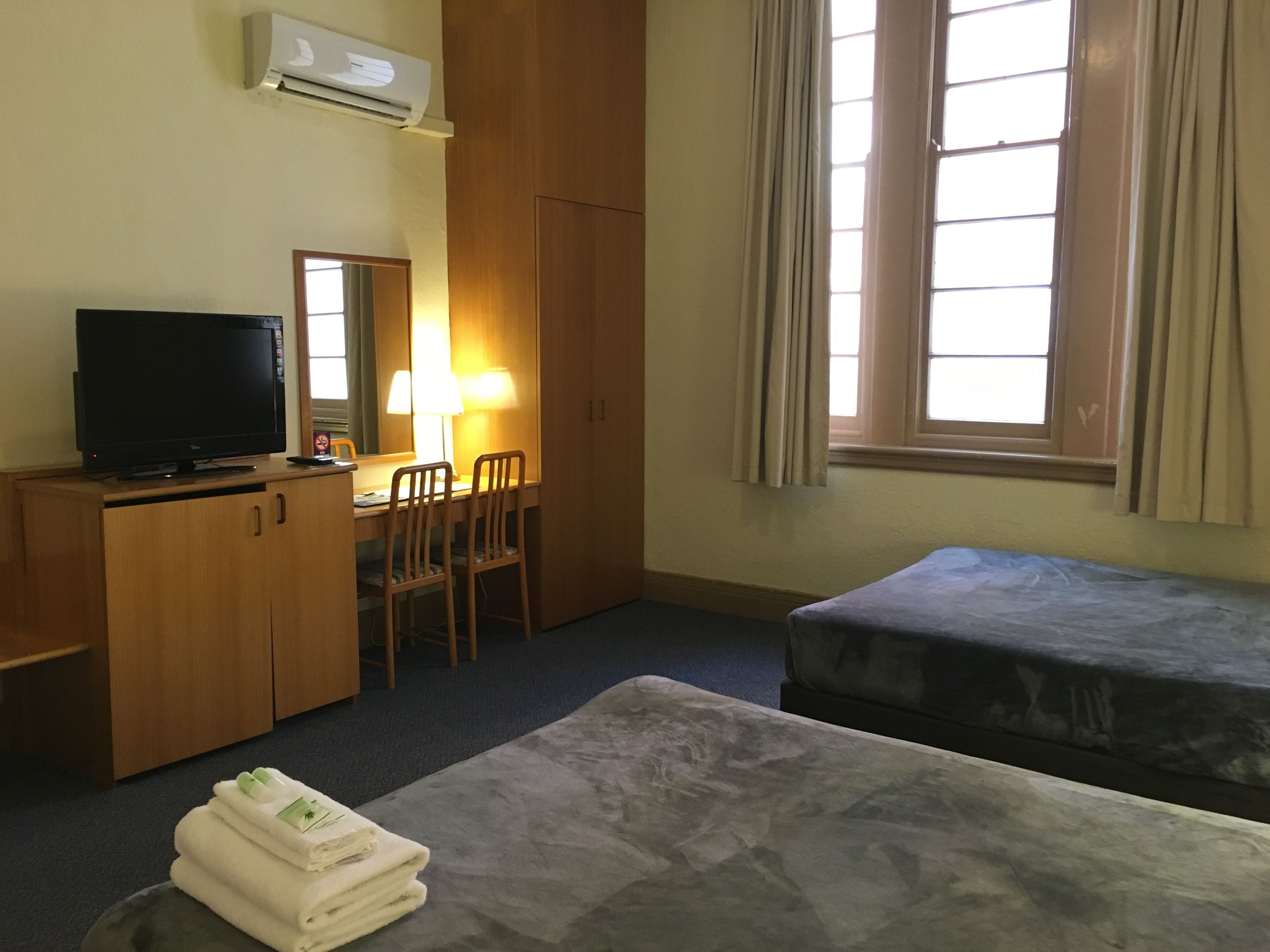 A hotel room with a TV, desk, chairs, a bed, and a window with curtains.