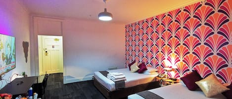 A hotel room with two beds, a desk, a chair, a ceiling fan, and a patterned wall.