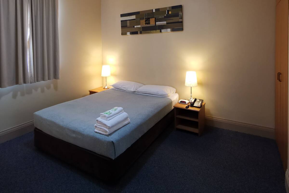 A hotel room with a bed, two bedside tables with lamps, a wall clock, and a ceiling light.