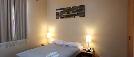 A hotel room with a bed, two bedside tables with lamps, a wall clock, and a ceiling light.