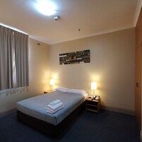 Una habitación de hotel con una cama, dos mesitas de noche con lámparas, un reloj de pared y una lámpara de techo.