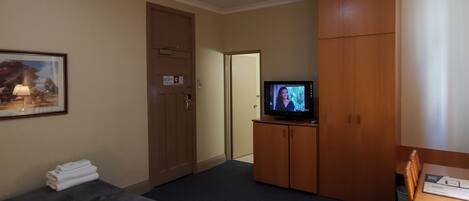 A hotel room with a bed, a TV on a wooden cabinet, a door, and a framed picture on the wall.