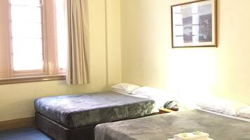 A hotel room with two beds, a window with curtains, a framed picture on the wall, and a small table with a phone and a book.