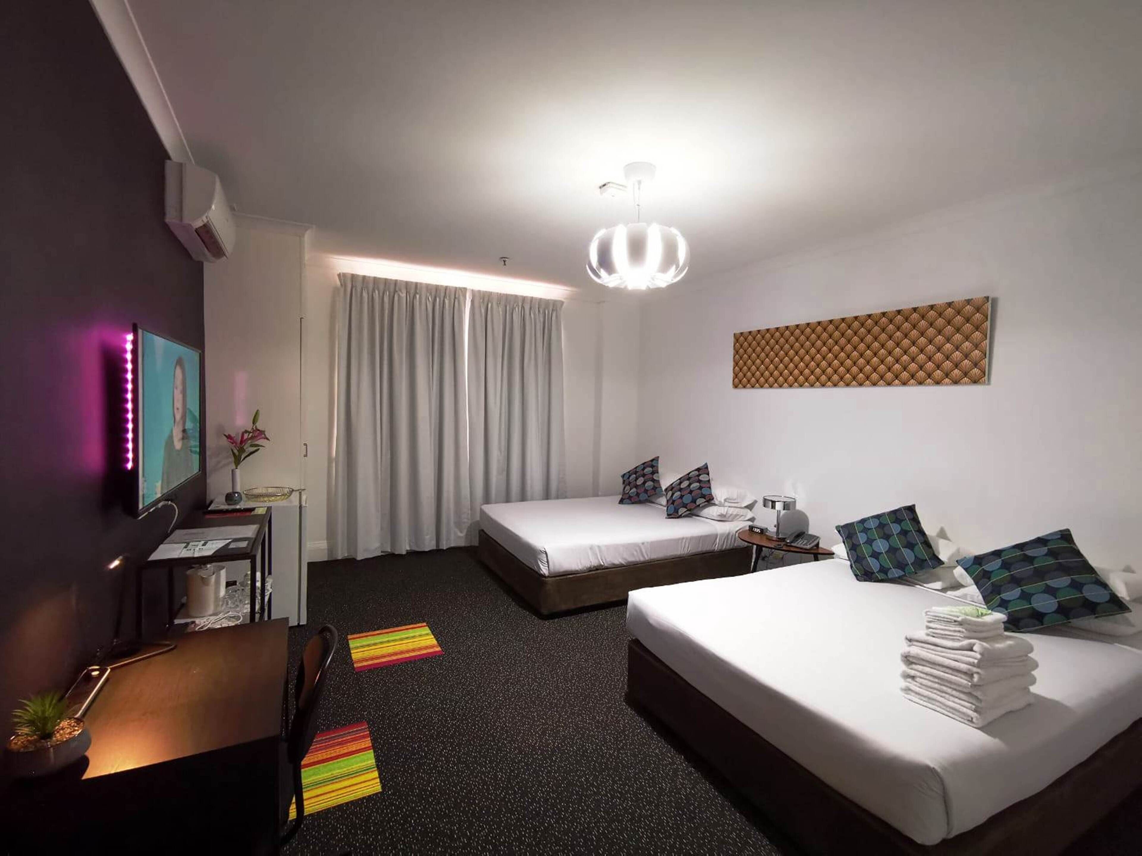 Une chambre d’hôtel avec deux lits, un bureau, une chaise, une télévision et un luminaire au plafond.