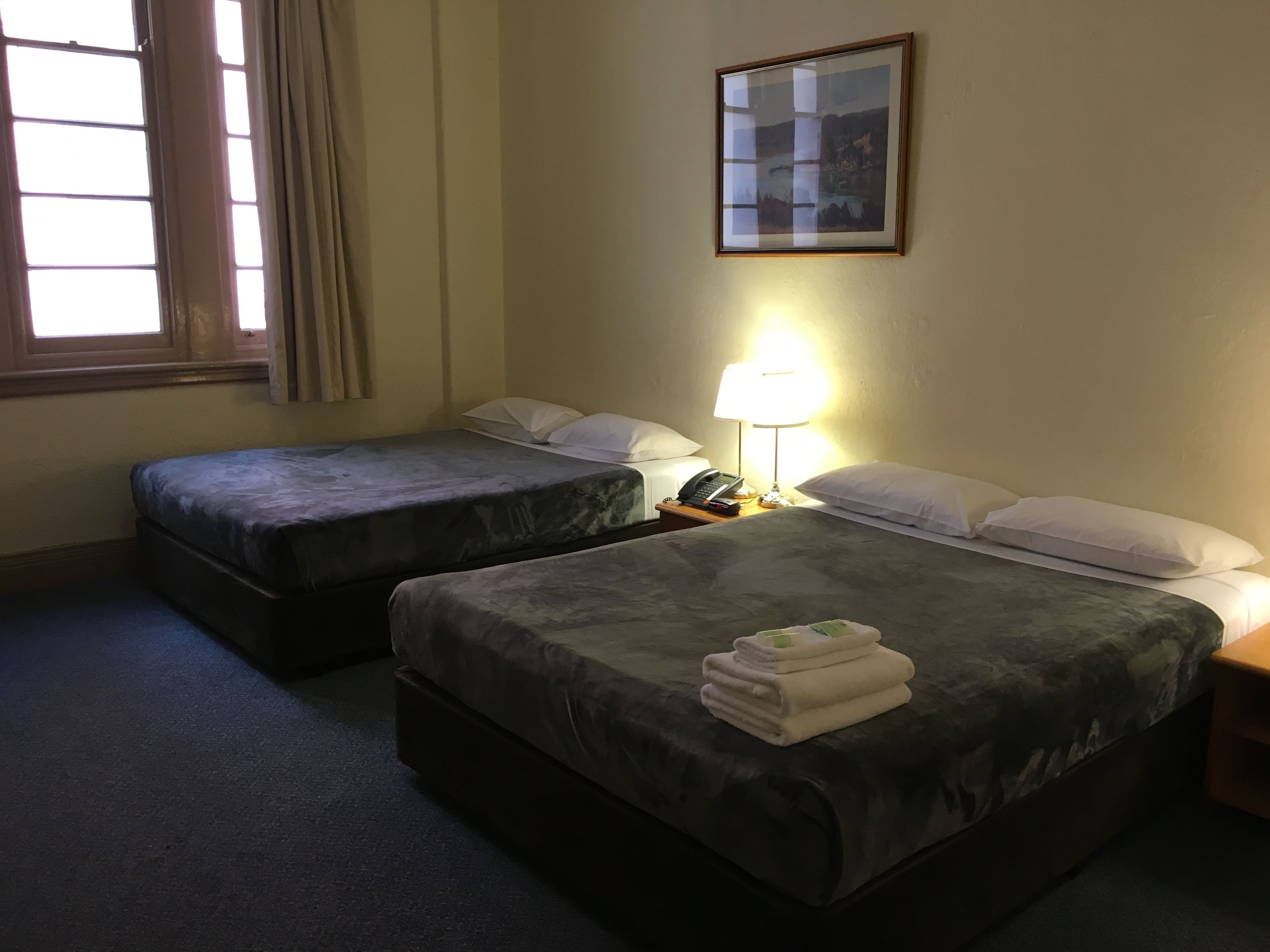 A hotel room with two beds, a nightstand with a lamp, and a framed picture on the wall.