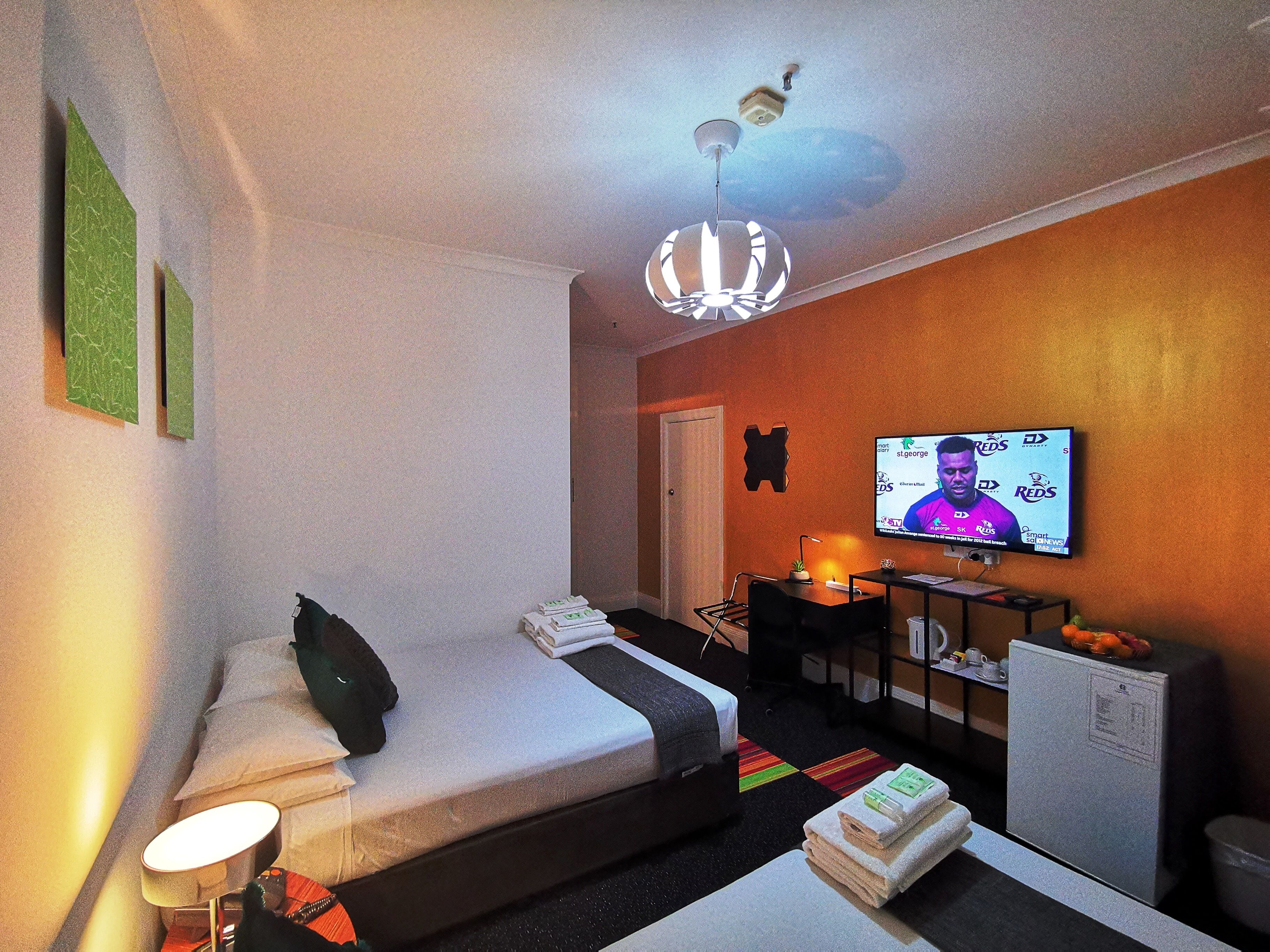 A hotel room with a bed, a desk, a television, and a ceiling fan.