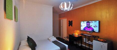 A hotel room with a bed, a desk, a television, and a ceiling fan.