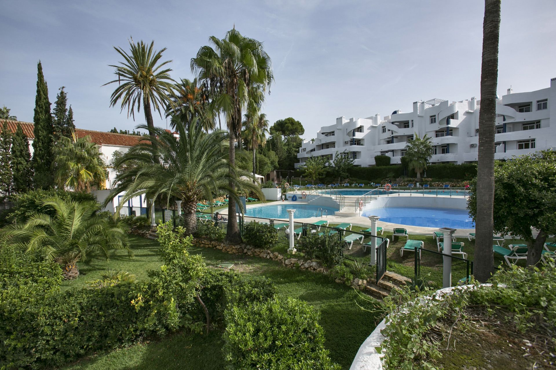 Um resort com várias piscinas, palmeiras e um edifício branco com varandas.