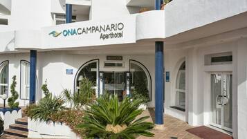 The exterior of ONACAMPANARIO apartment hotel with a reception area, potted plants, and a tiled entrance.