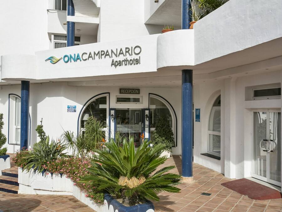 The exterior of ONACAMPANARIO apartment hotel with a reception area, potted plants, and a tiled entrance.