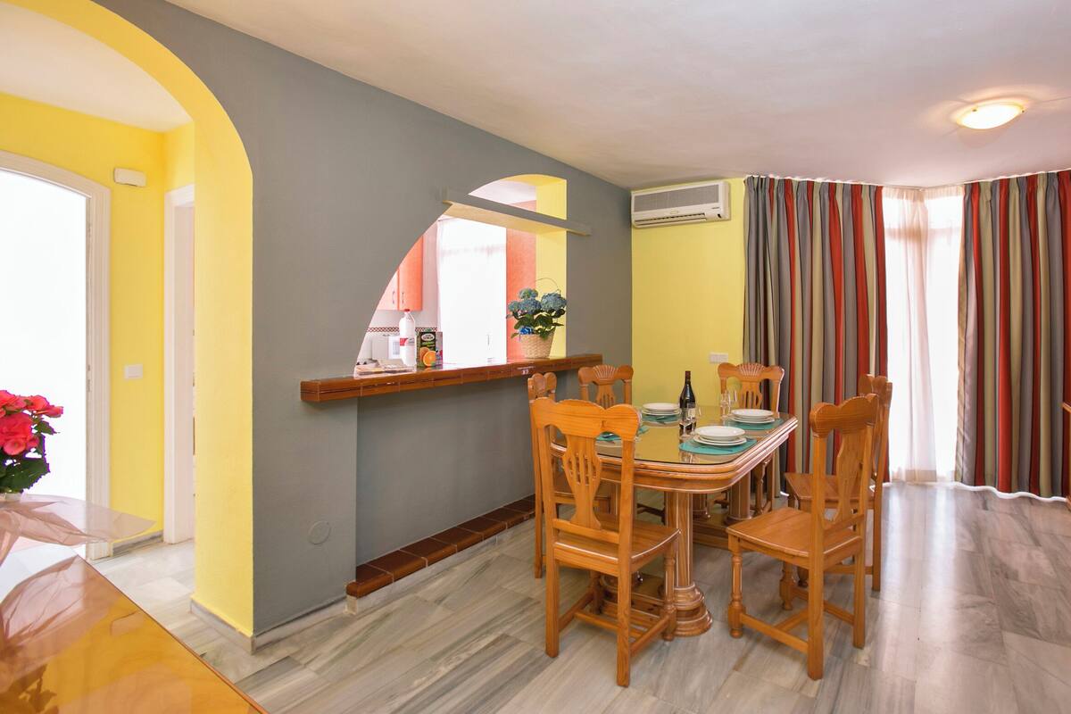 A dining area with a wooden table and chairs, a small window with a view, and a television on a wooden stand.