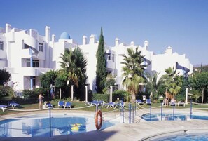 A resort with a swimming pool, palm trees, and white buildings with blue accents. - Apartamentos Ona Campanario (Mijas)