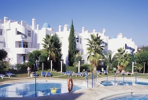 A resort with a swimming pool, palm trees, and white buildings with blue accents.