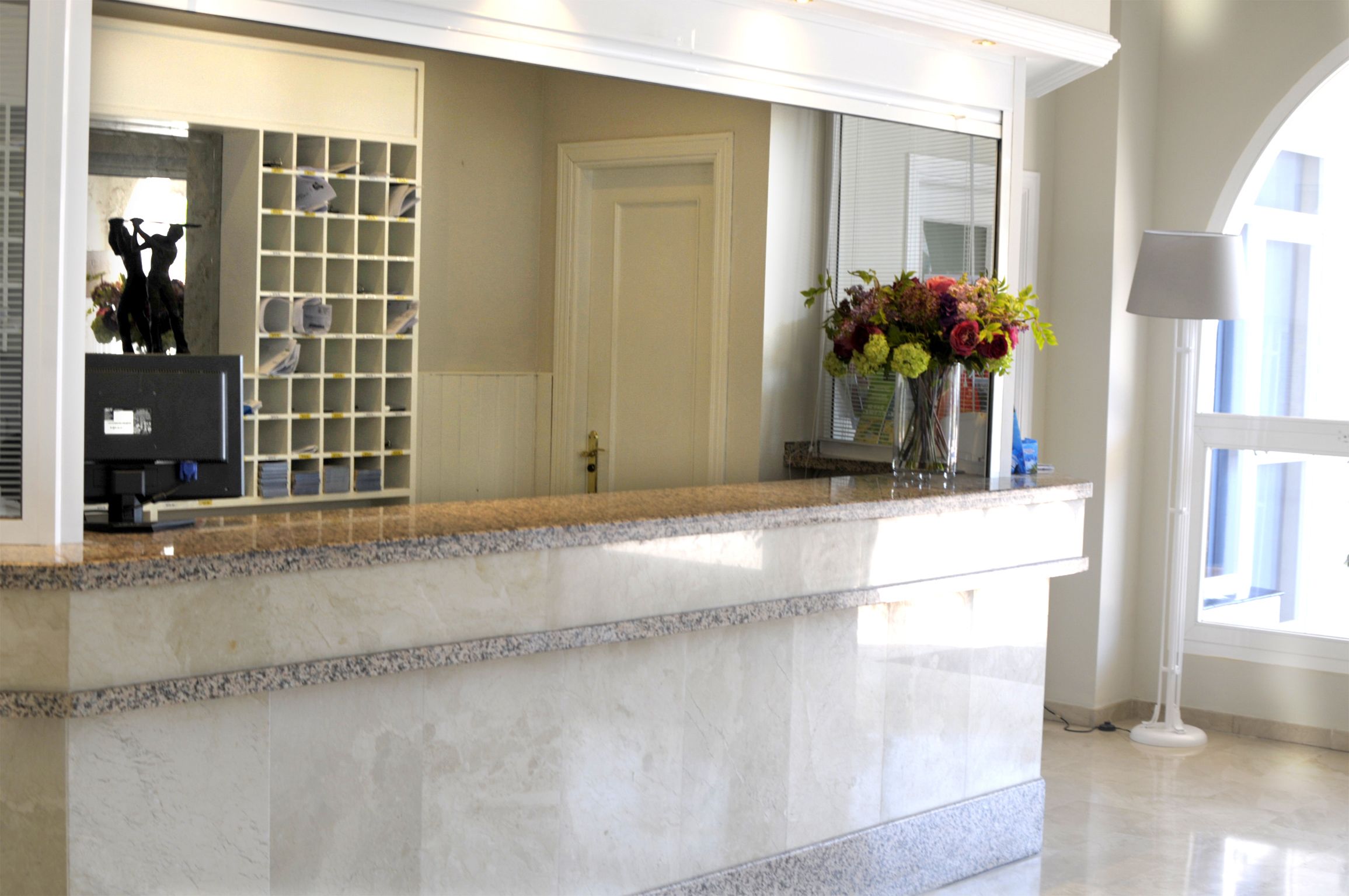 A reception area with a marble counter, a glass display case, a door, and a vase with flowers.