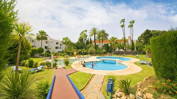 A resort with multiple swimming pools, palm trees, and lounge chairs. - Apartamentos Ona Campanario (Mijas)