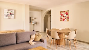 A modern living room with a grey sofa, a wooden coffee table, and a dining area with a wooden table and chairs. - Apartamentos Ona Campanario (Mijas)