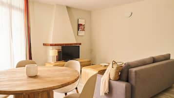 Una sala de estar moderna con una mesa redonda de madera, sillas color beige, un sofá gris y un televisor sobre un mueble de madera.