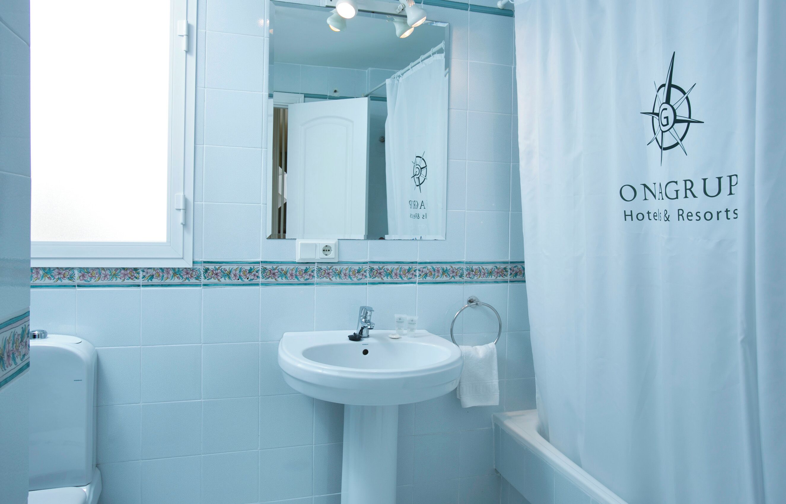A bathroom with a sink, mirror, and a towel rack. The walls are tiled in a light blue color.