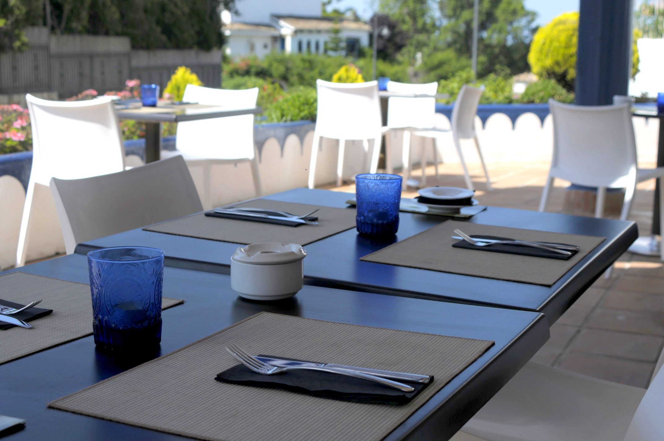 A dining area with tables set for two, featuring blue glassware, white plates, and black napkins.