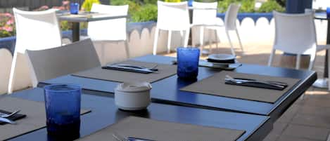 A dining area with tables set for two, featuring blue glassware, white plates, and black napkins.