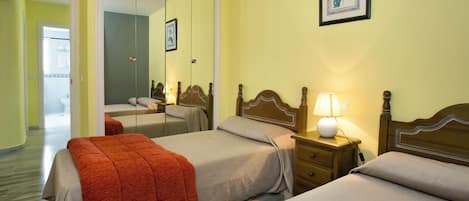 A hotel room with two beds, a bedside table with a lamp, a mirror, and a framed picture on the wall.