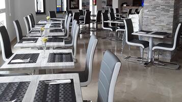 Un restaurant moderne doté de nombreuses tables et chaises, d’un mur décoratif en pierre et d’une cuisine ouverte visible au fond de la salle.