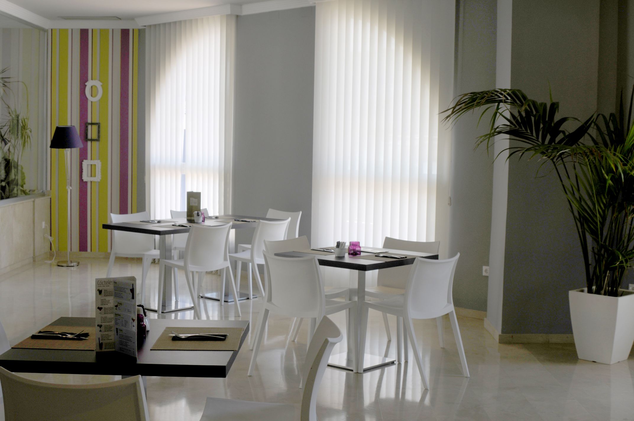 A modern dining area with white chairs and tables, a striped wall, and a potted plant.