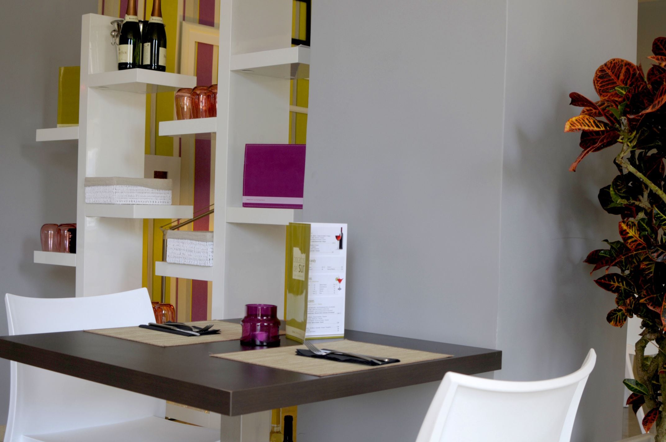 A dining area with a table, chairs, a menu, and a decorative plant.