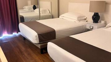 Quarto de hotel com duas camas, uma escrivaninha, uma cadeira, um espelho e duas imagens emolduradas na parede.