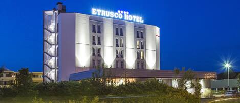 A hotel with a prominent sign reading "ETRUSCO HOTEL" against a twilight sky.