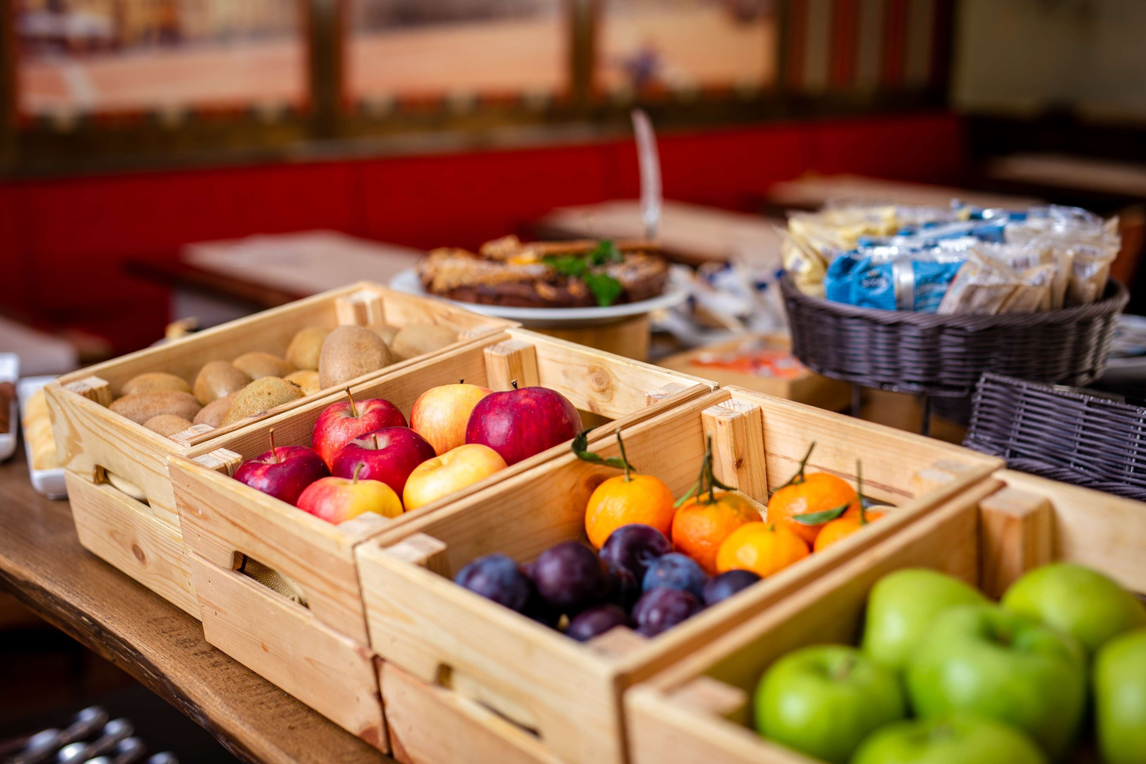 Wooden crates filled with fruits and vegetables, a basket of bread, and a plate of food in the background.