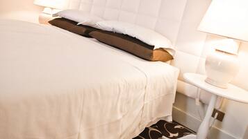 Una habitación de hotel con una cama grande, dos lámparas de noche, un cabecero blanco y una alfombra estampada.