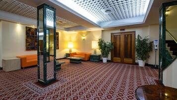 A lobby with patterned carpet, a reception desk, a sofa, a lamp, a potted plant, and a staircase.