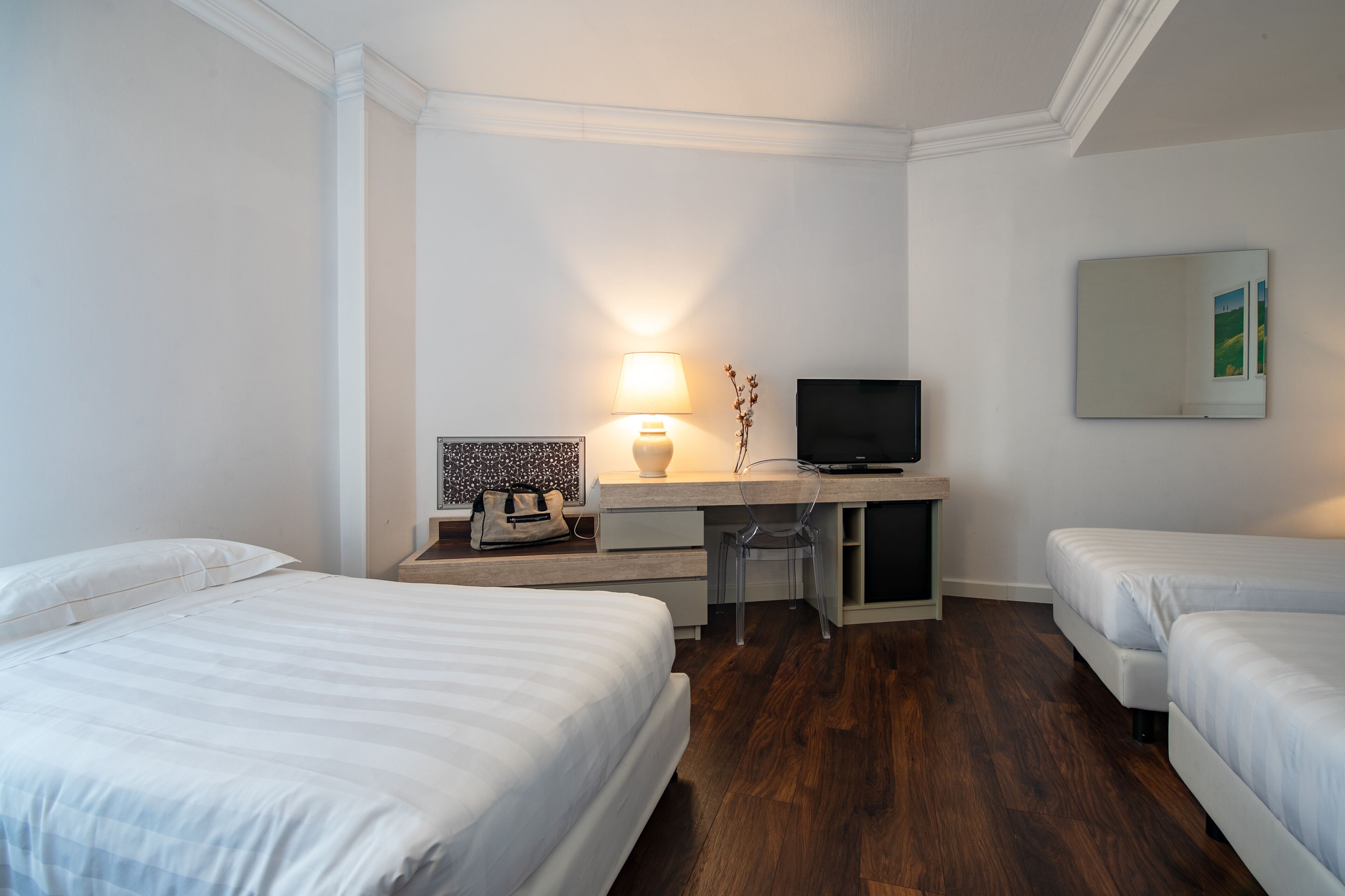 A hotel room with two beds, a desk with a TV, a lamp, and a mirror on the wall.