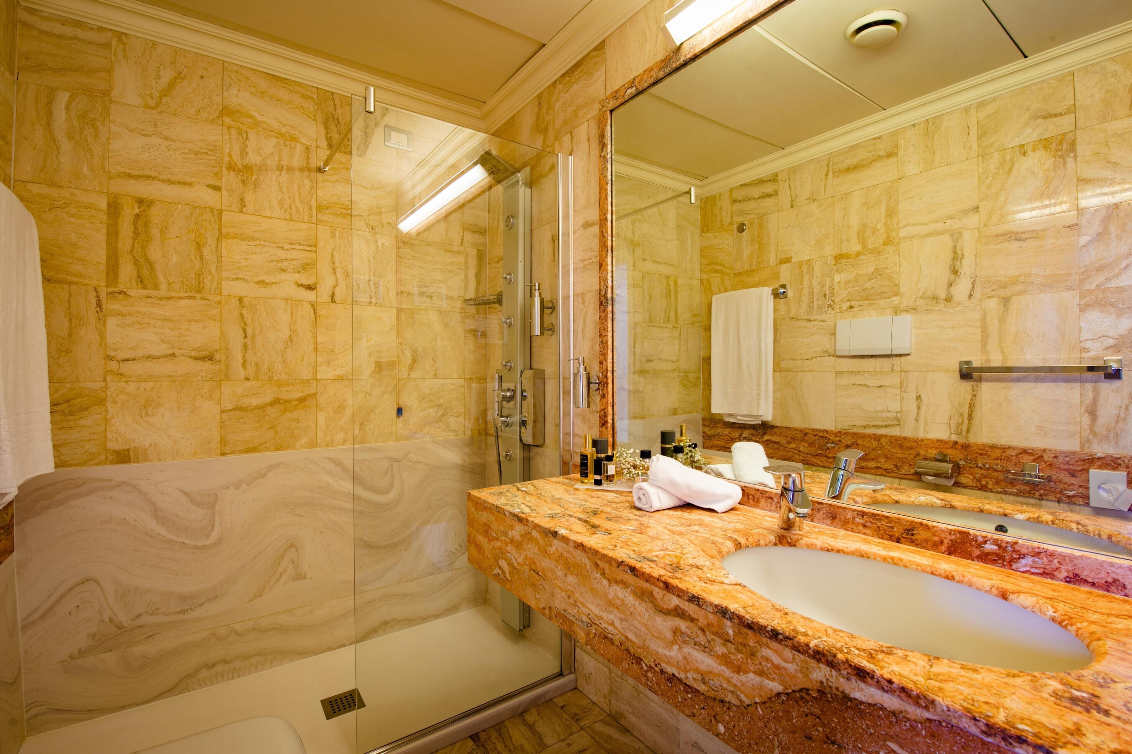 A bathroom with marble walls, a glass-enclosed shower, and a marble sink with a mirror.