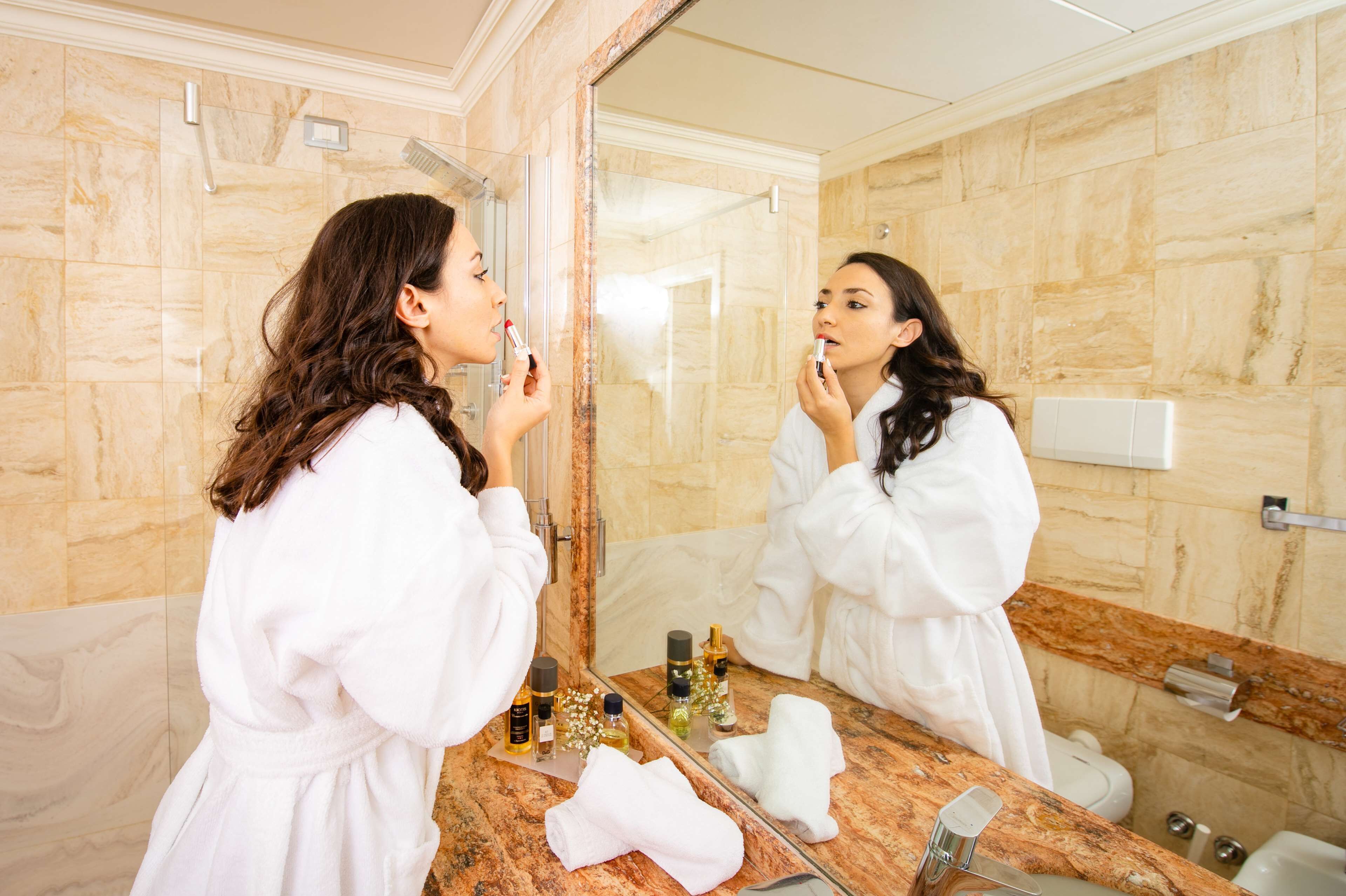A bathroom with a marble wall, a large mirror, and toiletries on the counter.
