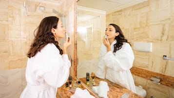 A bathroom with a marble wall, a large mirror, and toiletries on the counter.