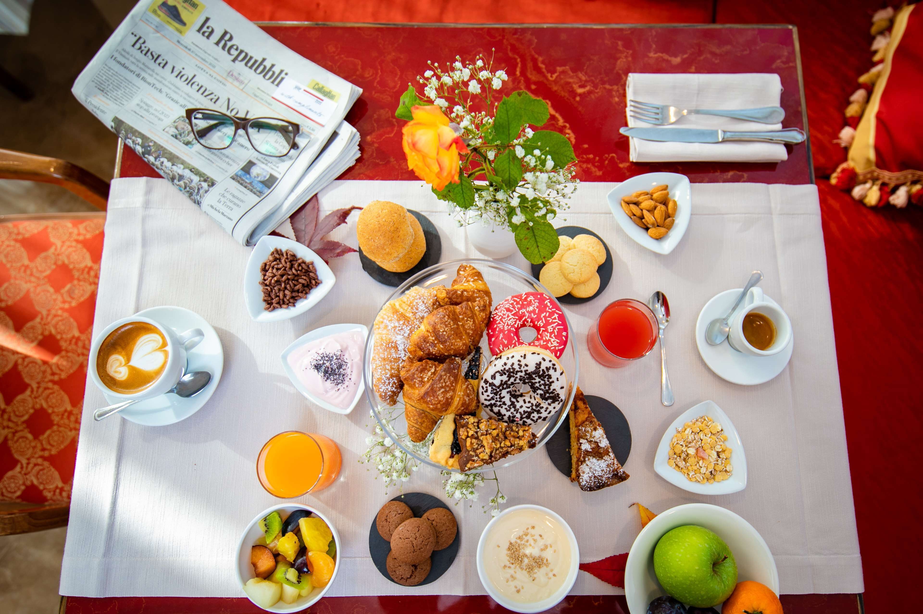 Uma mesa de café da manhã com diversos alimentos, um jornal e um vaso de flores.