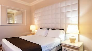 A hotel room with a large bed, two bedside tables with lamps, a mirror, and a padded headboard.