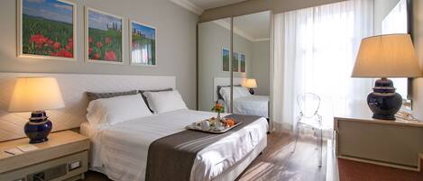 A hotel room with a large bed, bedside lamps, a tray of breakfast, and artwork on the walls.