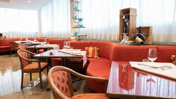 Een restaurant met rode bekleding, houten tafels en een decoratieve etagère met glazen.