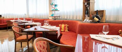 Un restaurante con asientos tapizados en rojo, mesas de madera y un expositor decorativo escalonado con copas.